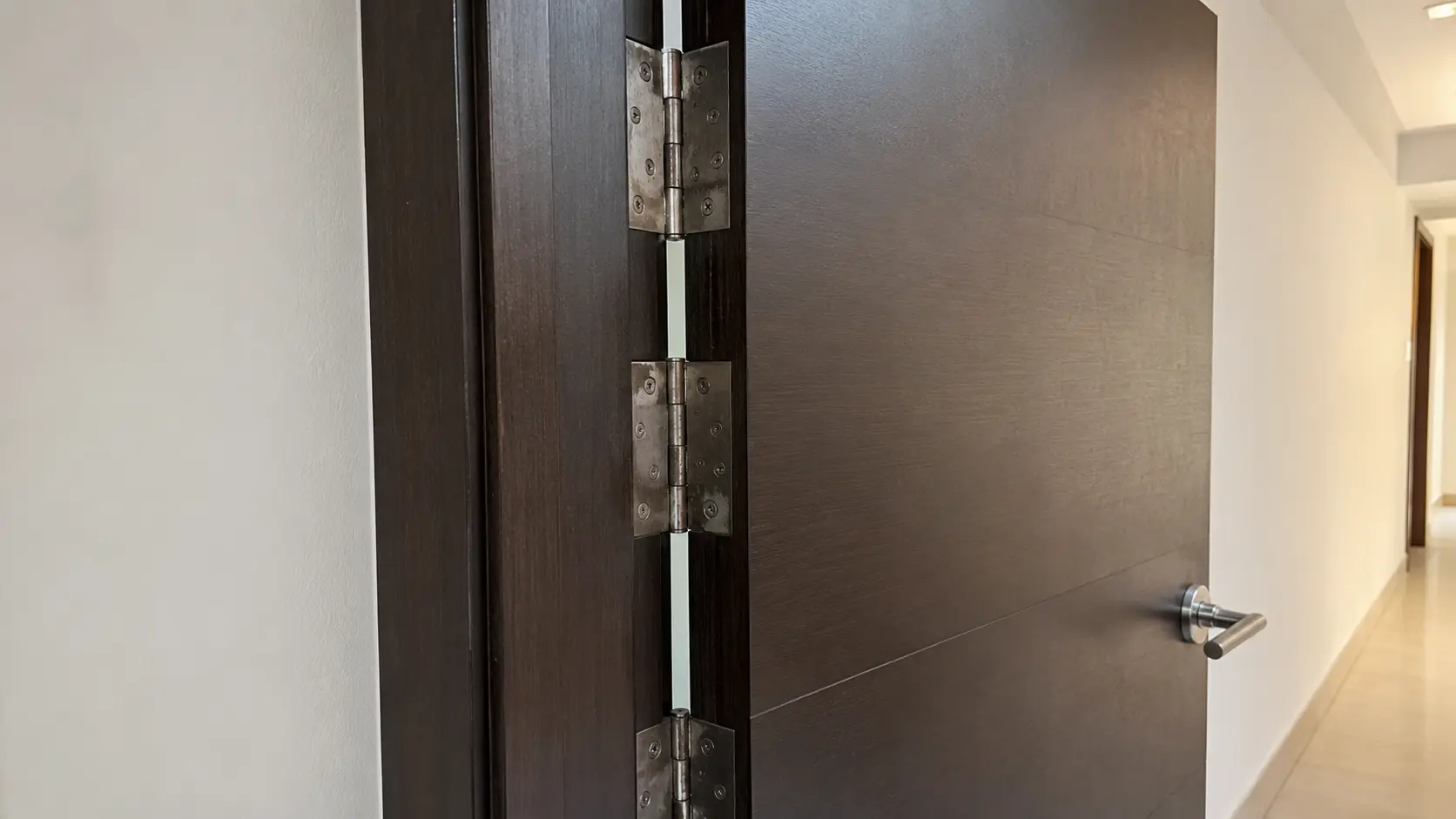 Close-up of a door frame gap and hinge area showing early signs of wear on a Singapore HDB main door